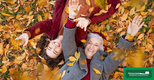 Two women laying in the fall foliage throwing leaves and laughing