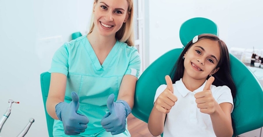 female dentist and pediatric patient smiling and holding thumbs up in a dental office
