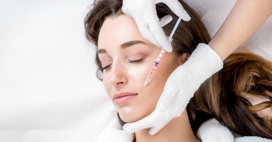 woman with brown hair laying down getting an injection in her cheek